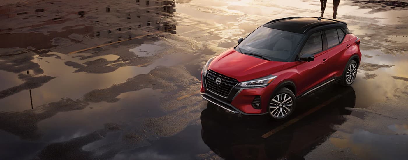 A red 2024 Nissan Kicks SR for sale is shown parked in lot after a rainstorm. 