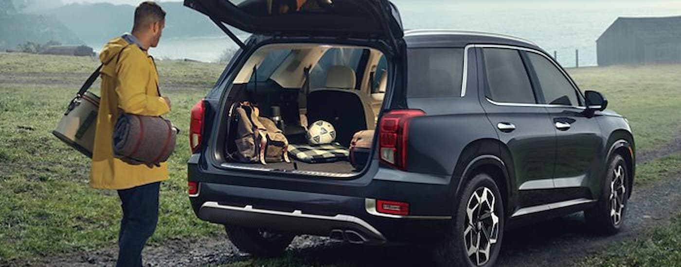A man is shown putting gear into the back of a dark blue 2021 Hyundai Palisade.