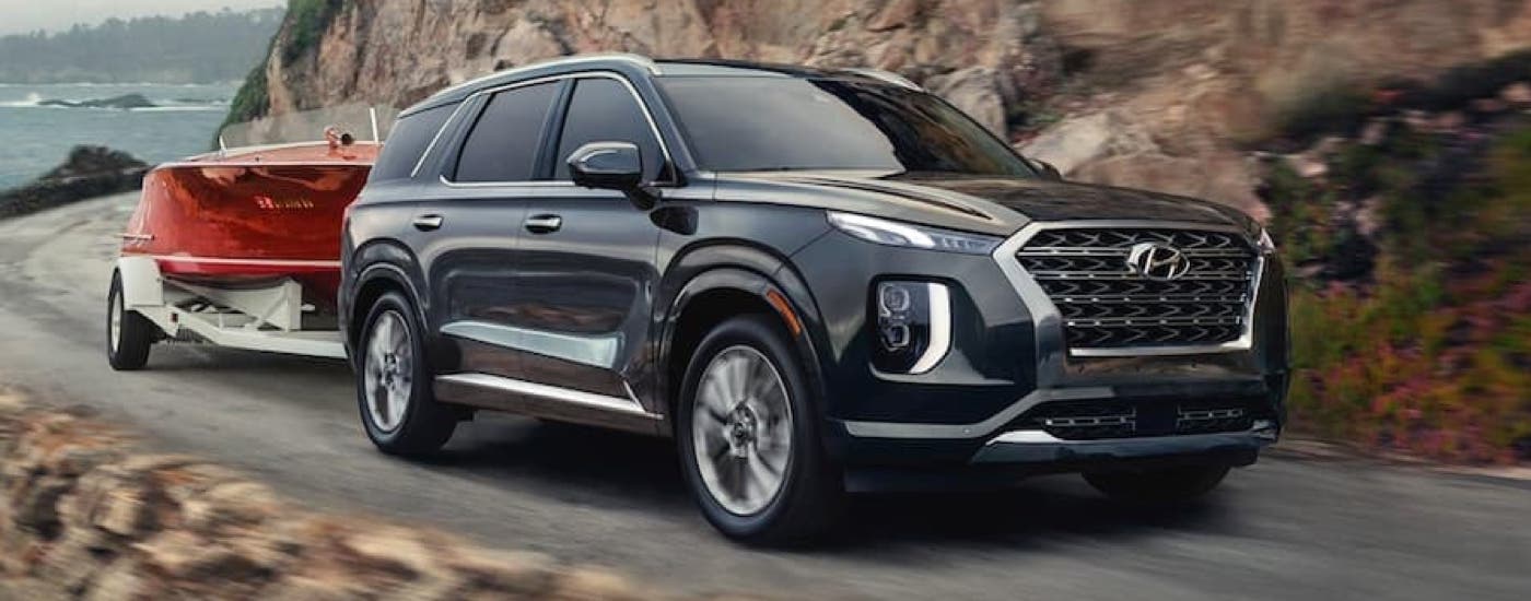 A black used 2020 Hyundai Palisade for sale is shown towing a red boat on a winding road.