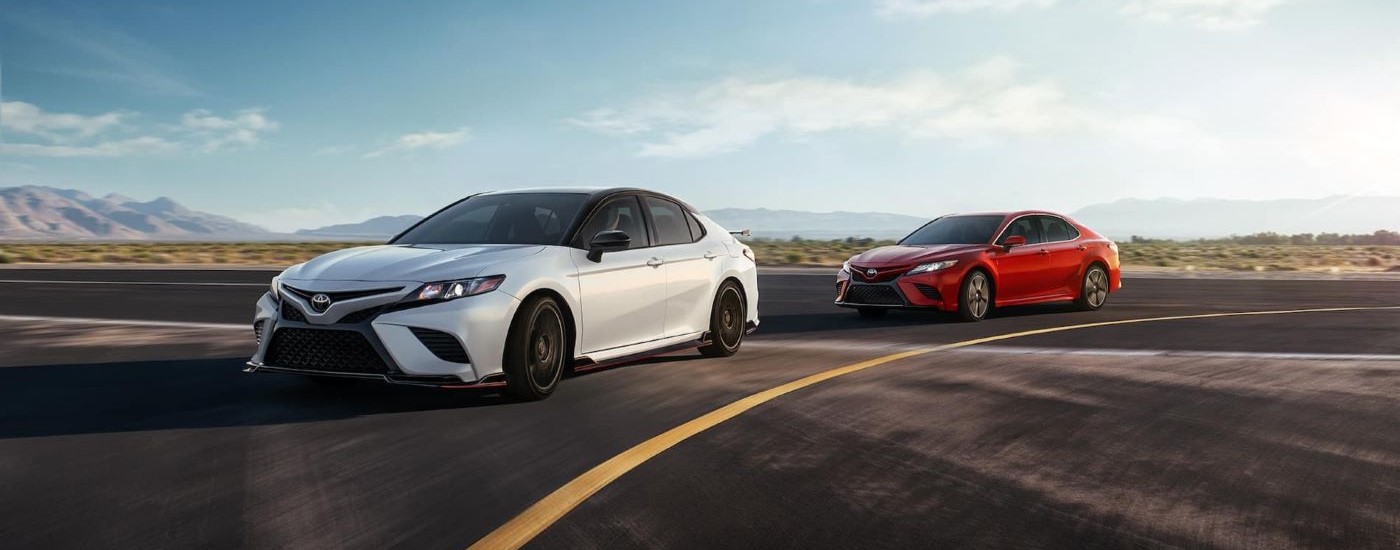 A white 2020 Toyota Camry TRD and a red Camry are shown rounding a corner on a race track.