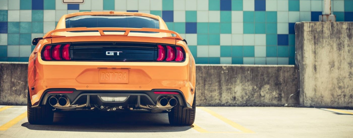 An orange  2018 Ford Mustang GT is shown from the rear near a tile wall.