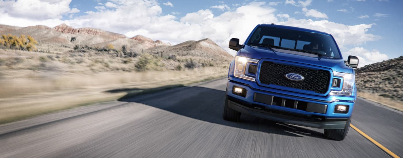 A blue 2018 Ford F-150 is shown driving on a highway after leaving a used car dealership.