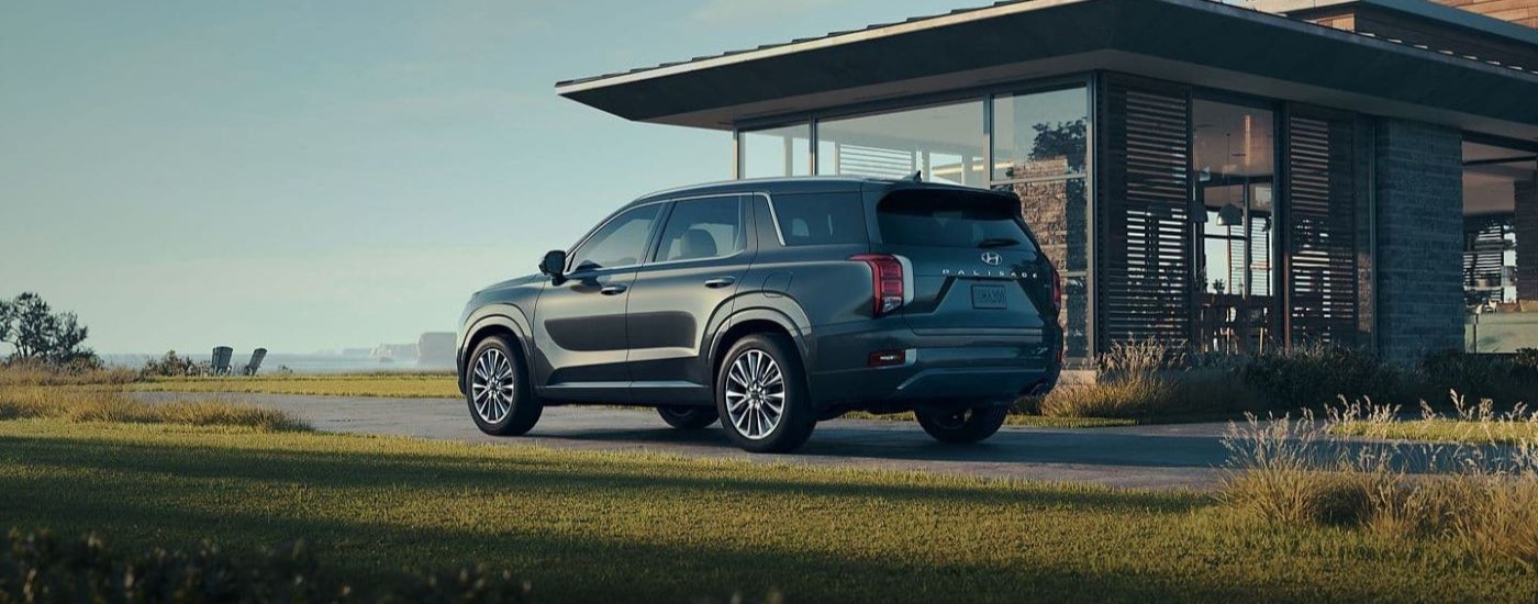 A close up shows a dark grey 2020 used Hyundai Palisade for sale parked on the driveway of a modern house.