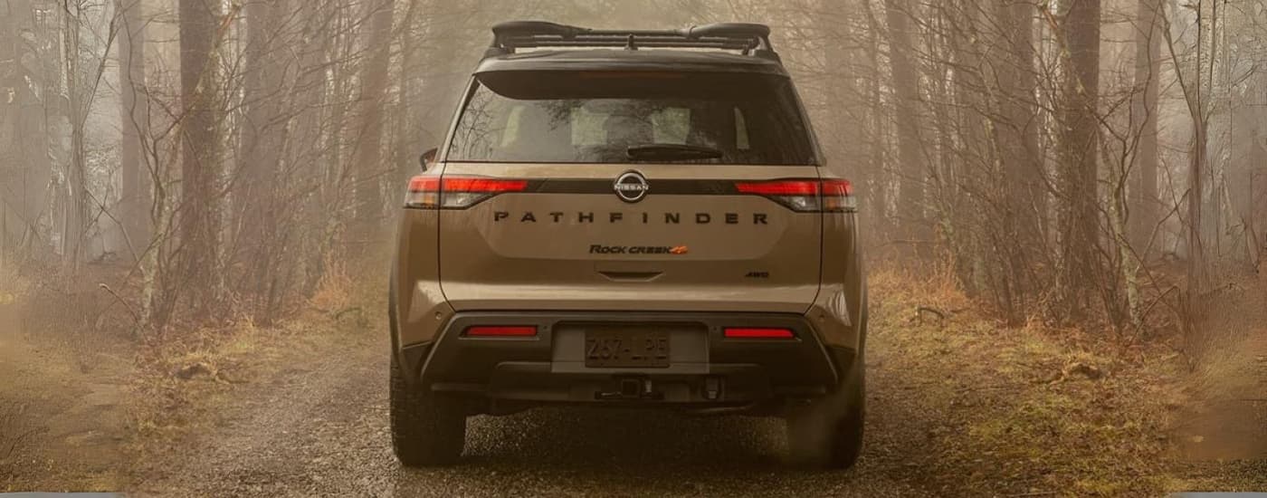 A tan 2024 Nissan Pathfinder Rock Creek is shown from behind on a foggy trail.