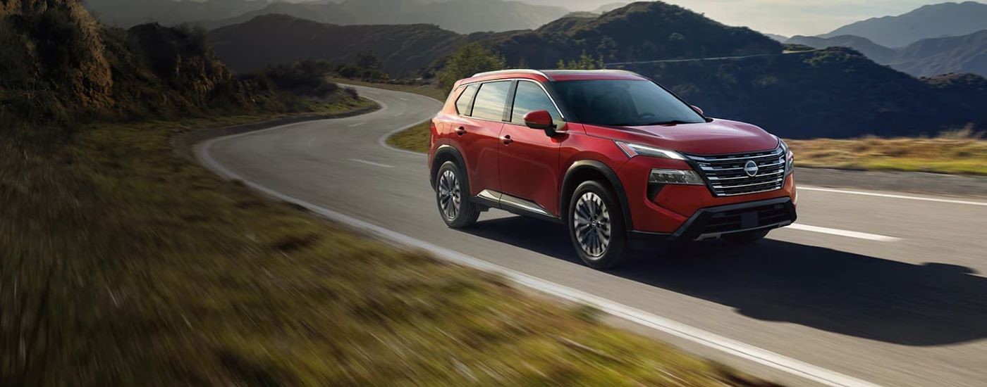 A red 2024 Nissan Rogue for sale is shown driving past distant mountains.