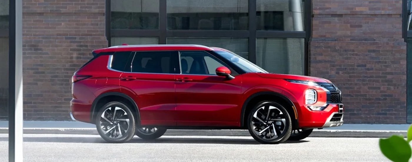 A red 2024 Mitsubishi Outlander for sale is shown from the side on a city street.
