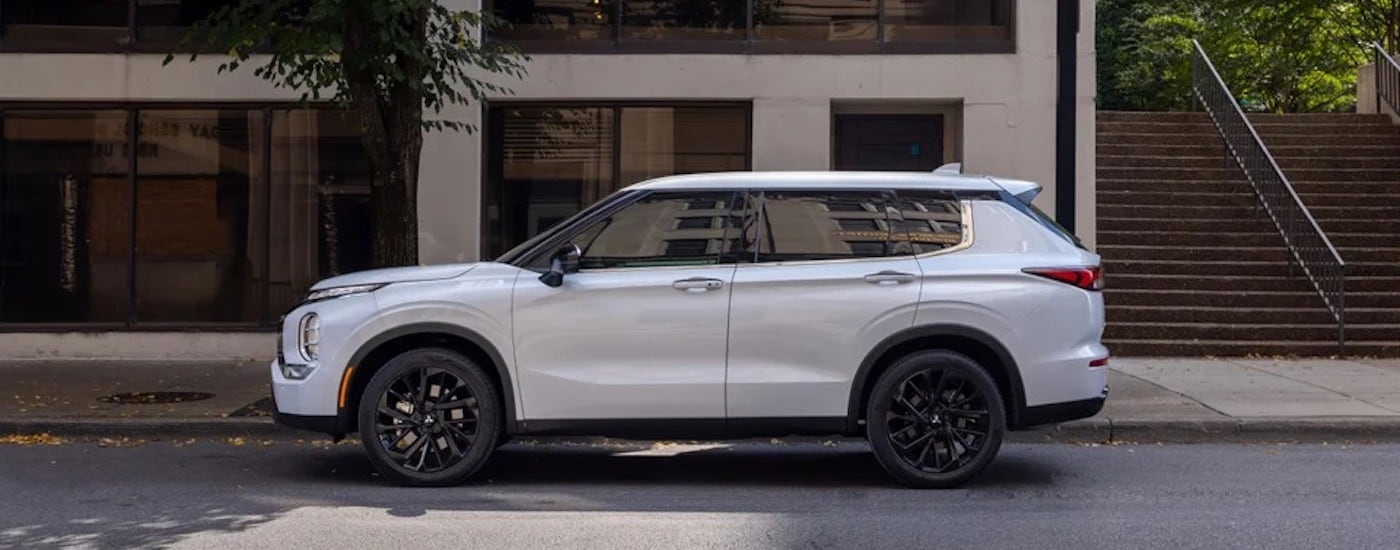A white 2024 Mitsubishi Outlander is shown from the side on a city street.