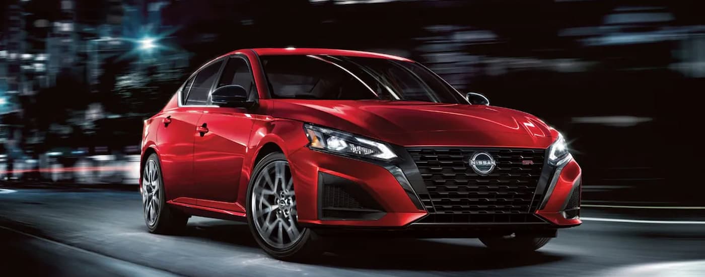 A red 2024 Nissan Altima SR is shown driving on a city highway at night.