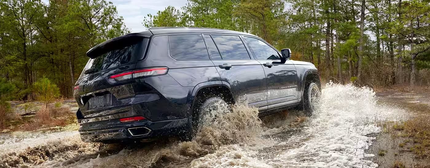 A grey 2024 Jeep Grand Cherokee L is shown from the rear at an angle while driving through mud after leaving a Jeep dealer.