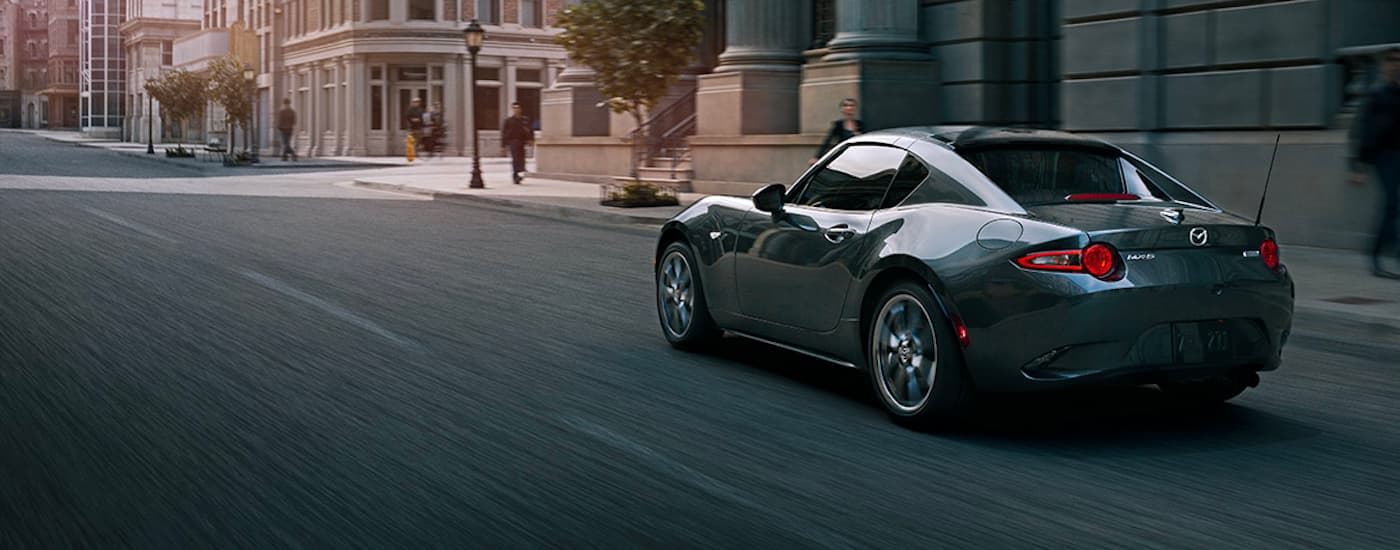 A grey 2022 Mazda MX-5 Miata RF is shown from behind driving on a city street.