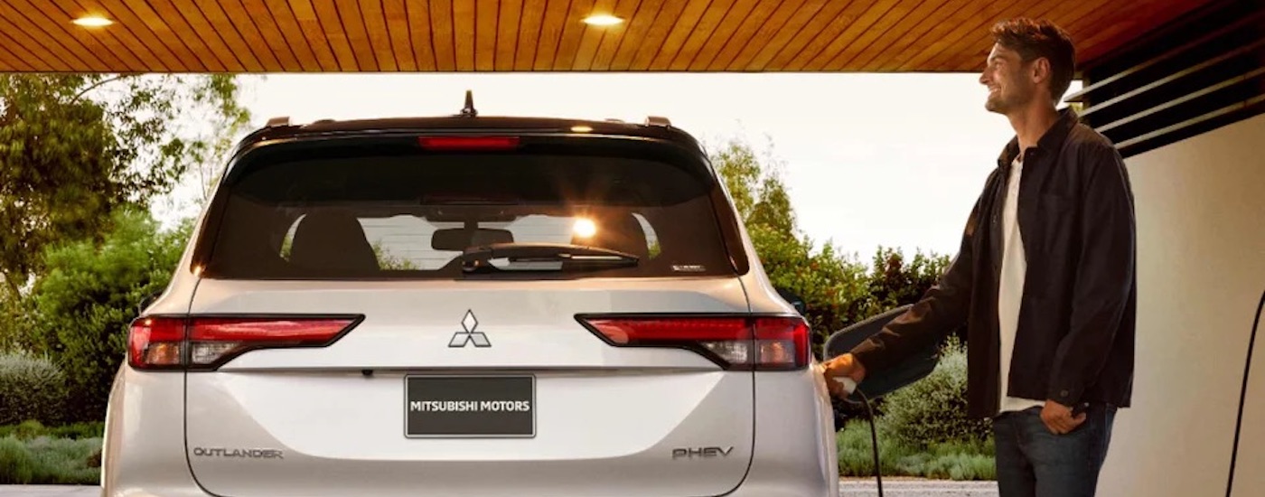A man is shown plugging in a white 2024 Mitsubishi Outlander PHEV.