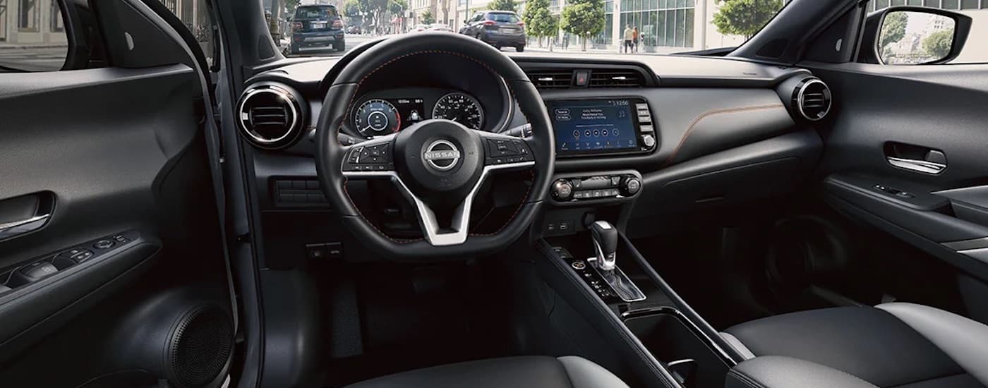 The grey interior of a 2024 Nissan Kicks for sale is shown from the driver's seat.
