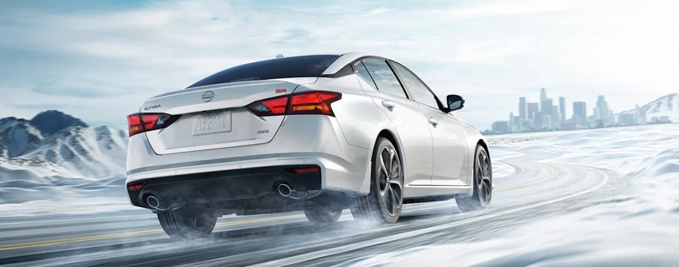 A white 2024 Nissan Altima SR is shown from the rear at an angle on a snowy road after leaving a dealer that has a Nissan Altima for sale.