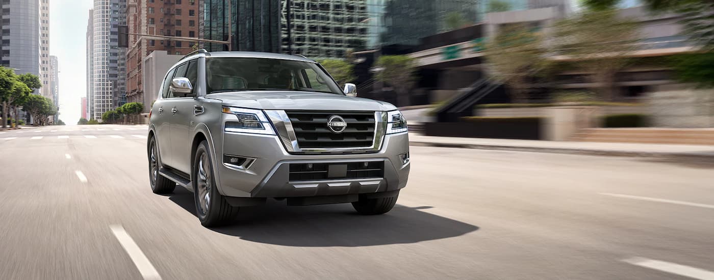 A silver 2023 Nissan Armada Platinum for sale is shown driving on a city street.