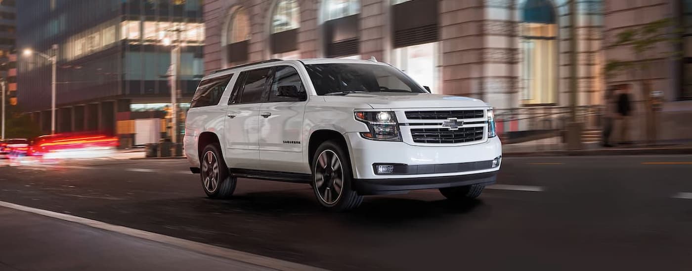 A white 2020 Chevy Suburban is shown driving on a city street at night.