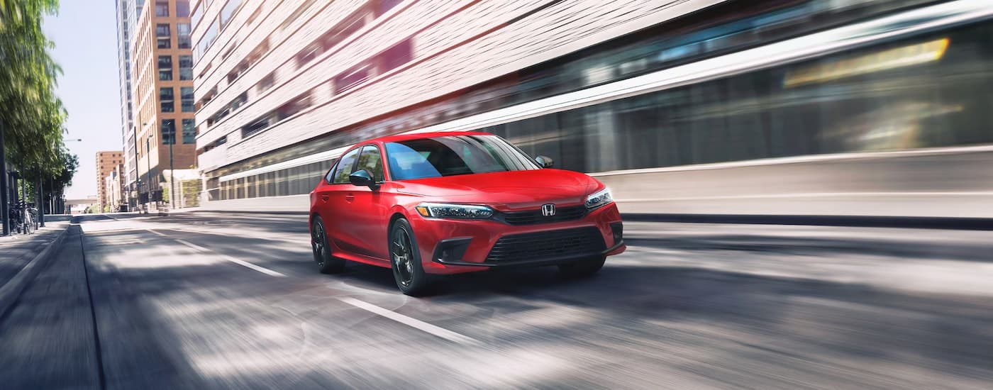 A red 2024 Honda Civic Sport is shown driving on a city street.