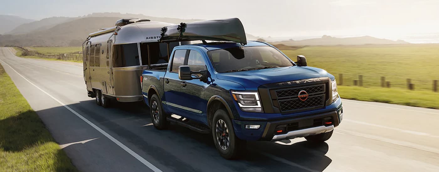 A blue 2024 Nissan Titan Crew Cab is towing a silver camper trailer on an open road.