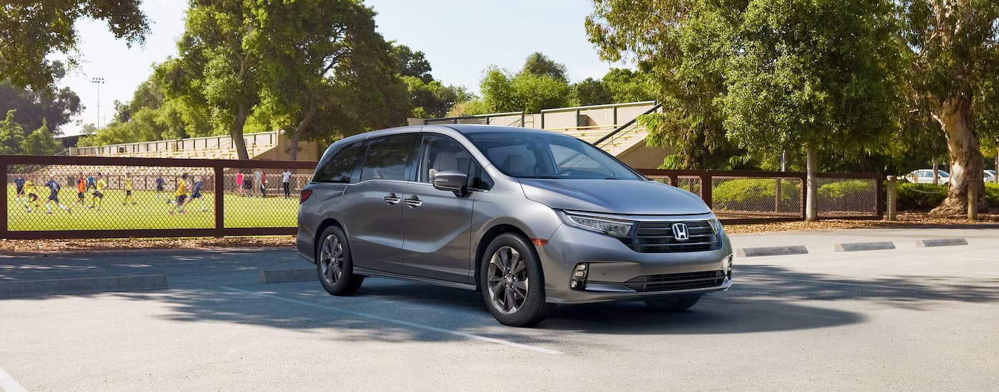 A grey 2024 Honda Odyssey Elite is parked near a sports field.
