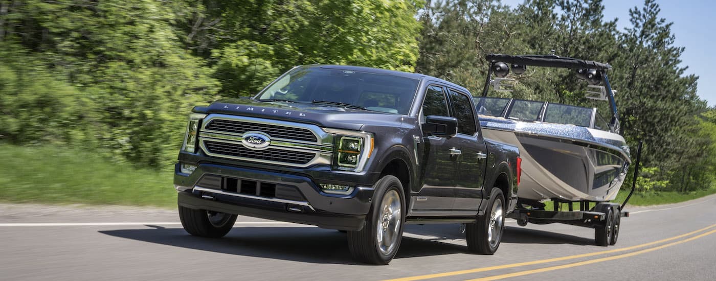 A grey 2022 Ford F-150 Limited is shown from the front at an angle while towing a boat after leaving a used truck dealer.
