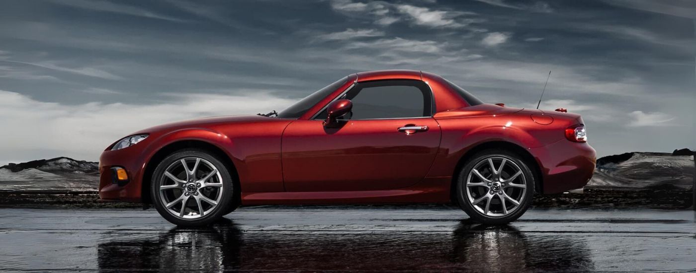 A red 2014 Mazda MX-5 Miata is shown from the side on a cloudy day.