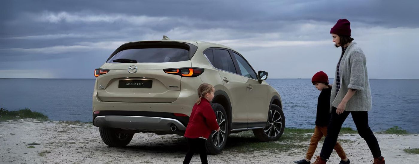 A green 2023 Mazda CX-5 is shown next to a family near an ocean.