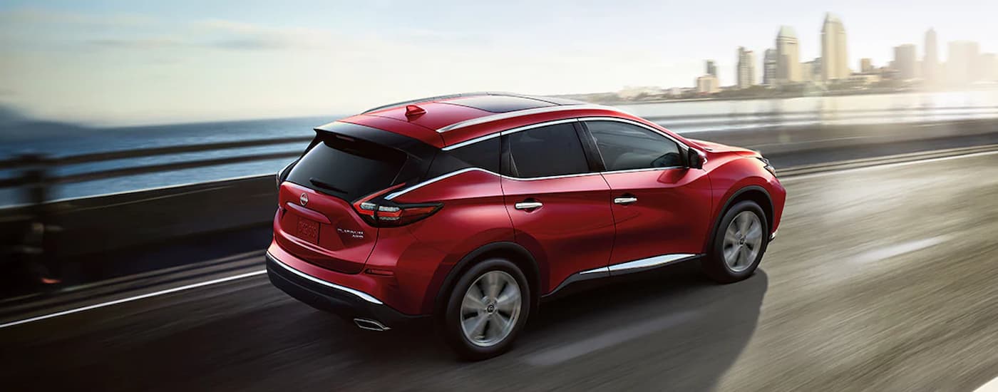 A red 2024 Nissan Murano is driving on a highway towards a city.