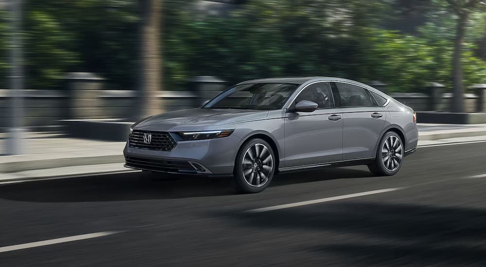 A grey 2024 Honda Accord Touring Hybrid for sale is driving on a street.