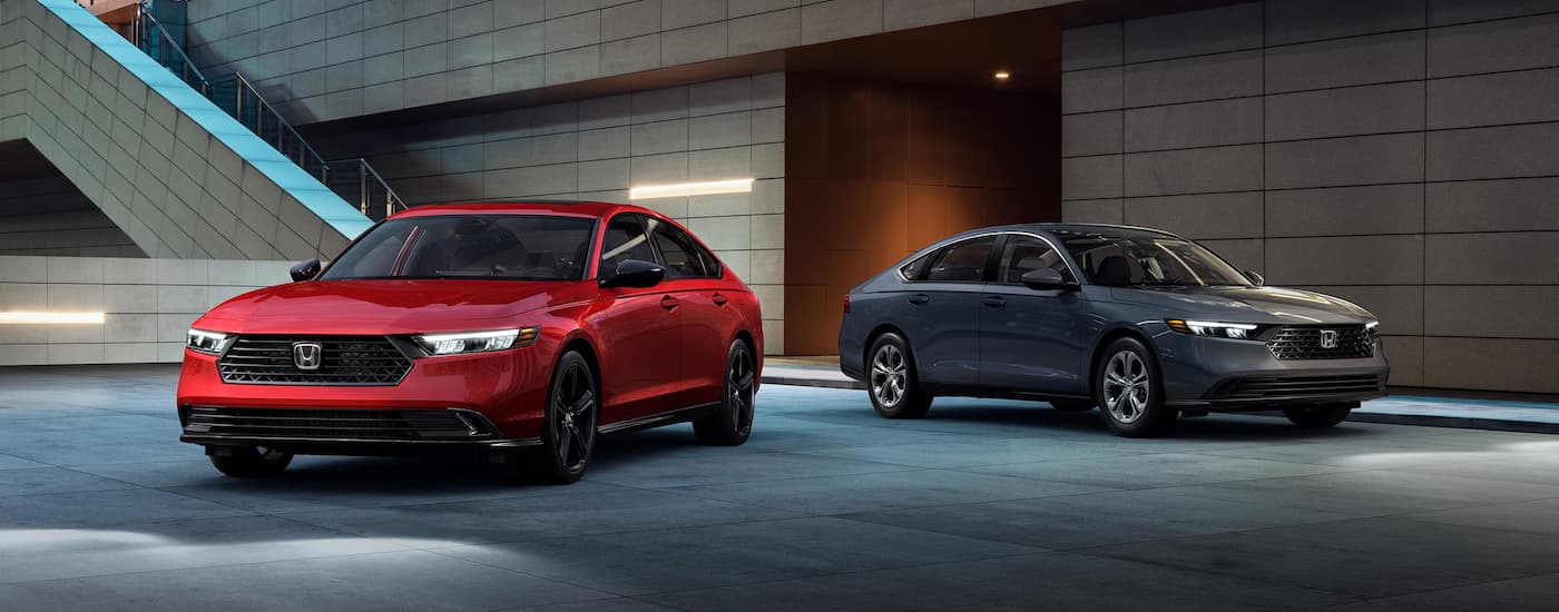 A red and grey 2024 Honda Accord Sport Hybrid are parked at night near a building.