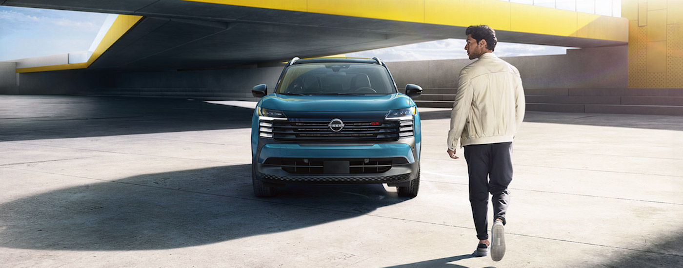A man is shown walking up to a blue 2025 Nissan Kicks SR from the front.