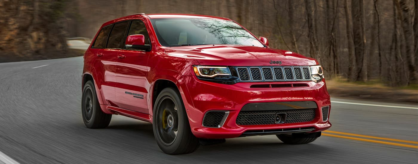A red 2021 Jeep Grand Cherokee Trackhawk is driving on a winding road to a used car dealer near Shiprock.