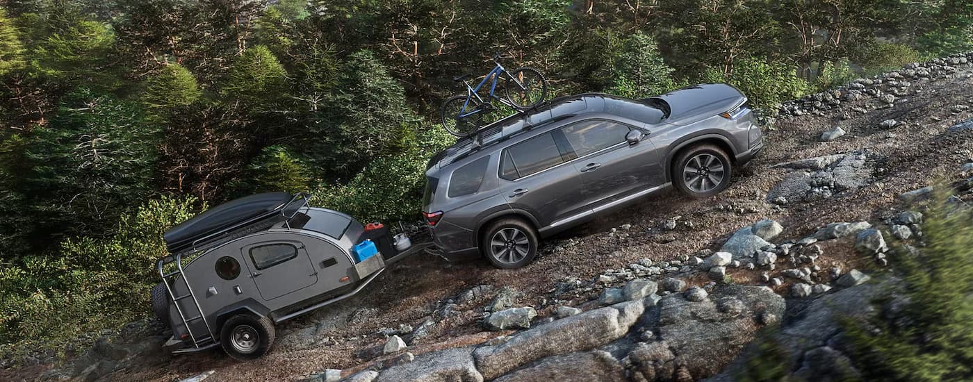 A grey 2025 Honda Pilot is towing a camper trailer up a rocky trail.