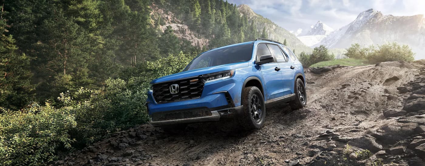 A blue 2025 Honda Pilot Trailsport off-roading on a muddy trail.