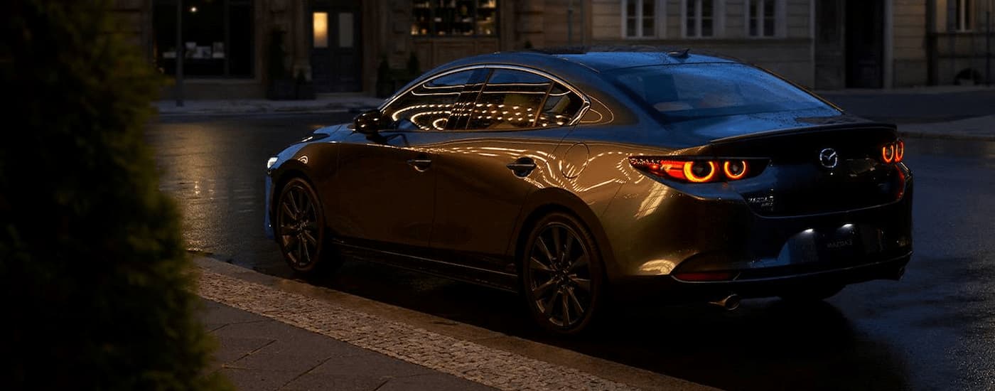 A grey 2024 Mazda 3 Sedan is parked on the side of a city street at night.
