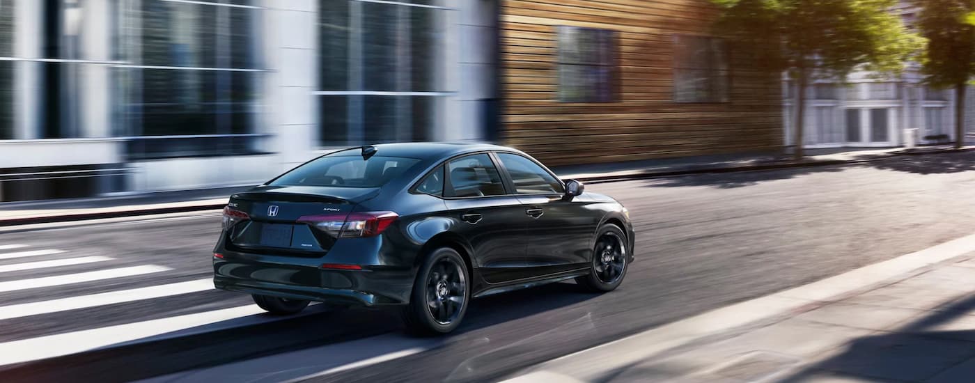 A black 2025 Honda Civic Sport Hybrid is driving on a city street.