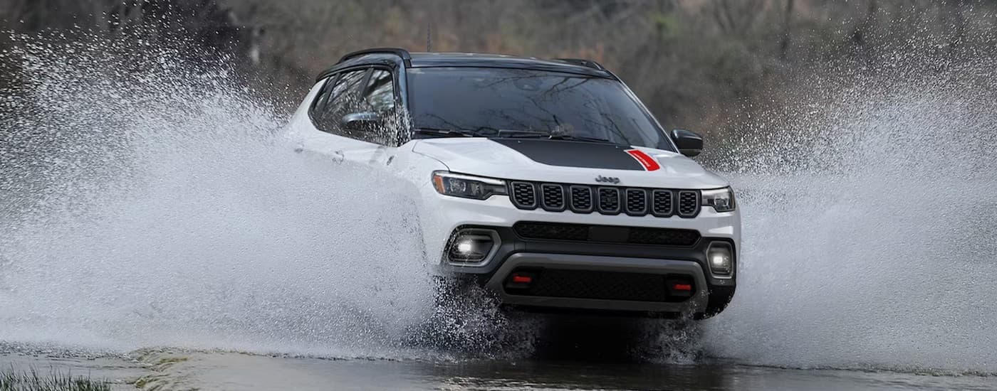 A white 2023 Jeep Compass Trailhawk is shown from the front while driving through water.