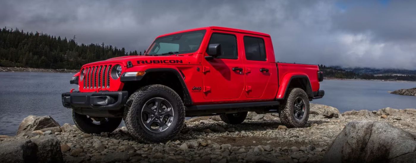 A red 2023 Jeep Gladiator Rubicon parked near a lake.