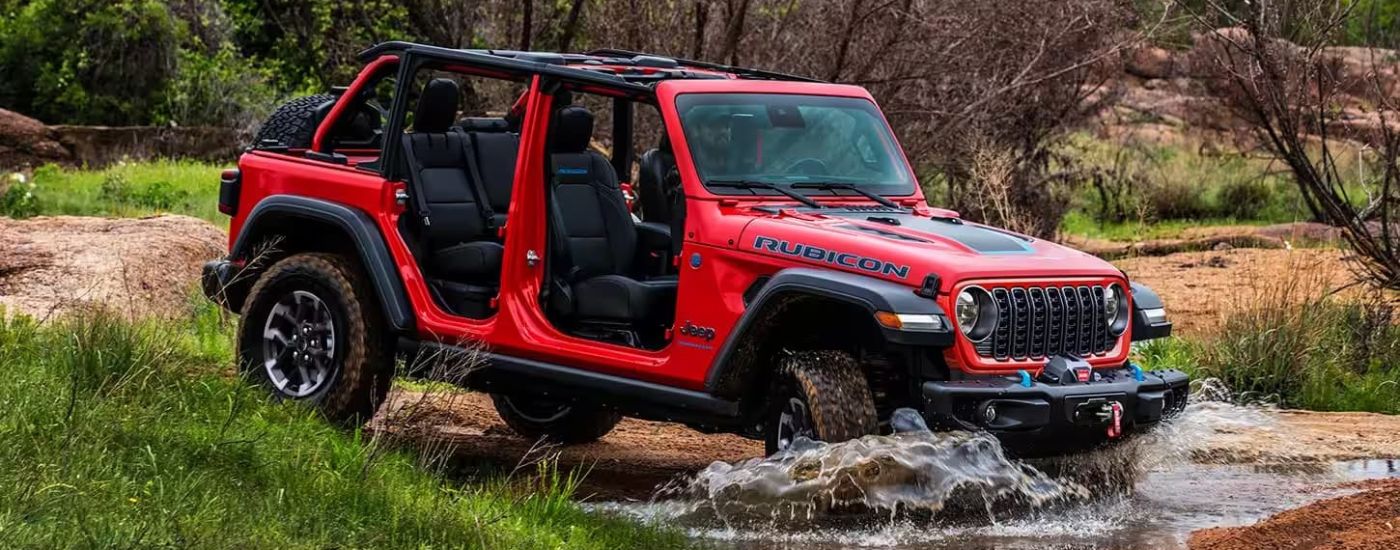 A red 2024 Jeep Wrangler 4xe Rubicon driving though a creek.
