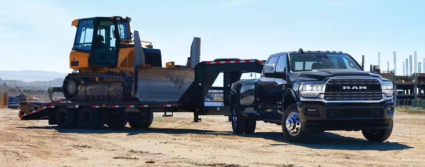 A black 2023 Ram 3500 towing a bulldozer at a construction site.