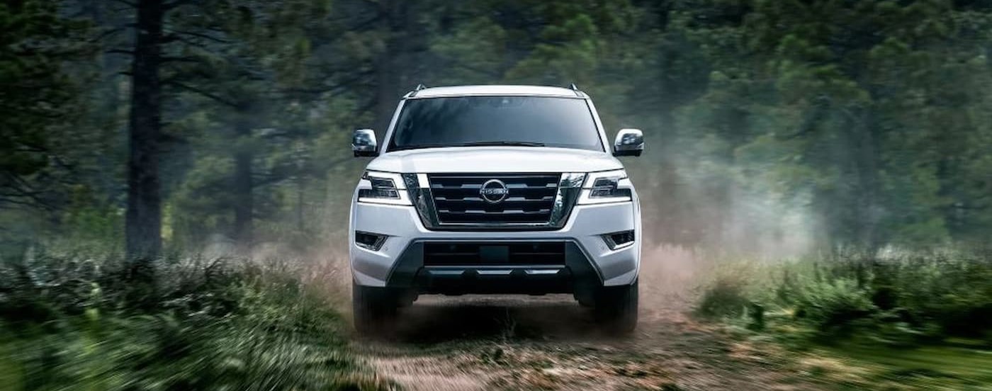 A white 2024 Nissan Armada is shown driving on a dirt path in a forest.