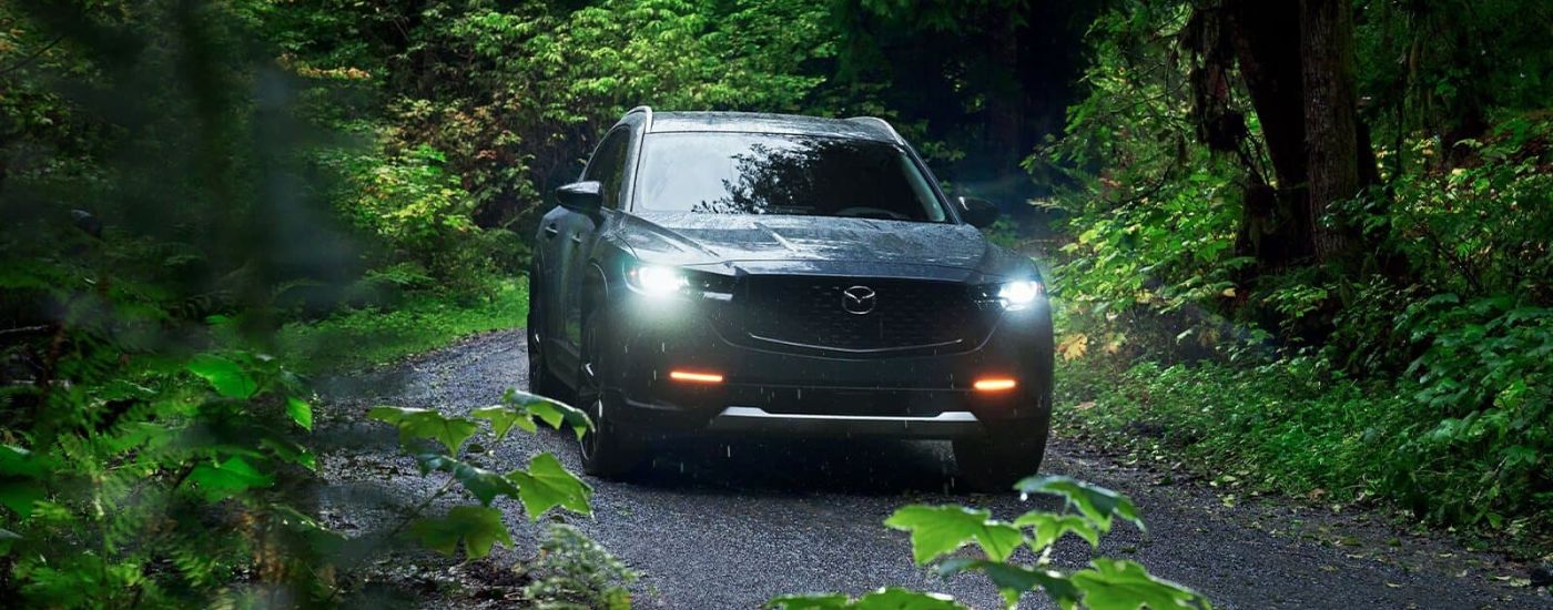 A grey 2024 Mazda CX-50 for sale is shown driving on a trail.