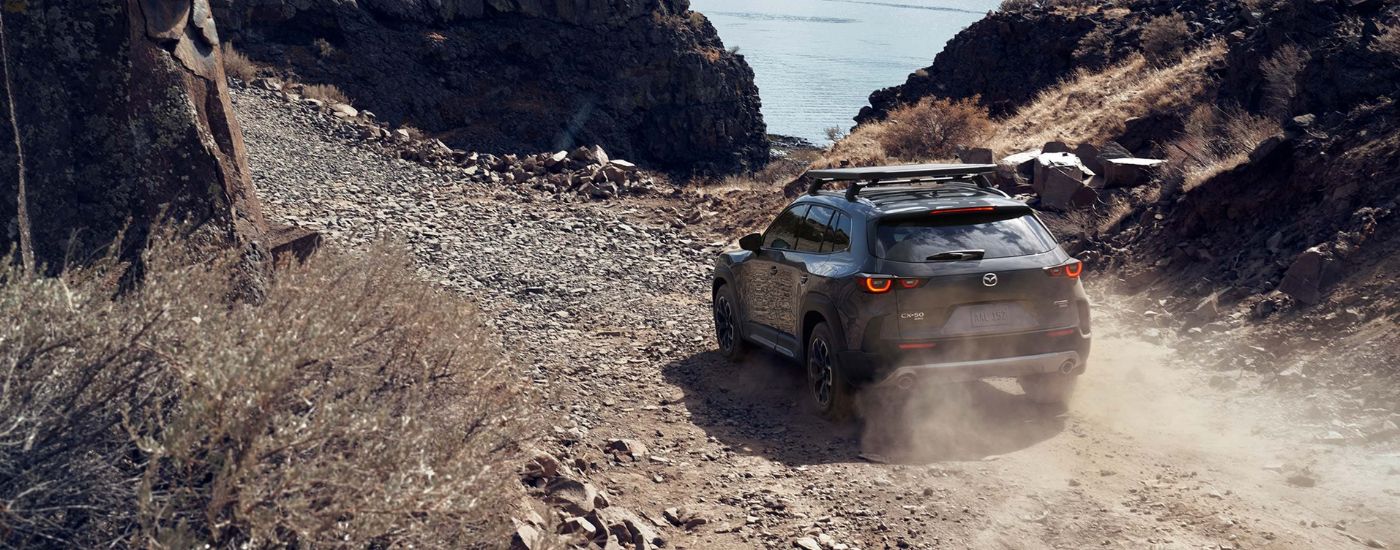 A dark grey 2024 Mazda CX-50 is shown driving on a rocky trail.