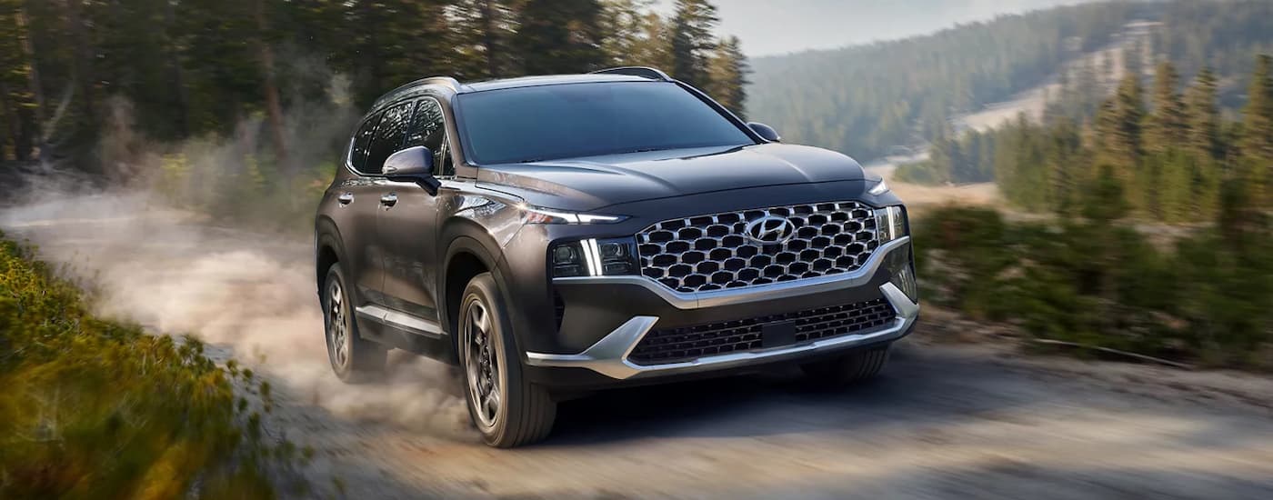 A grey 2022 Hyundai Santa Fe is driving on a dusty dirt road.