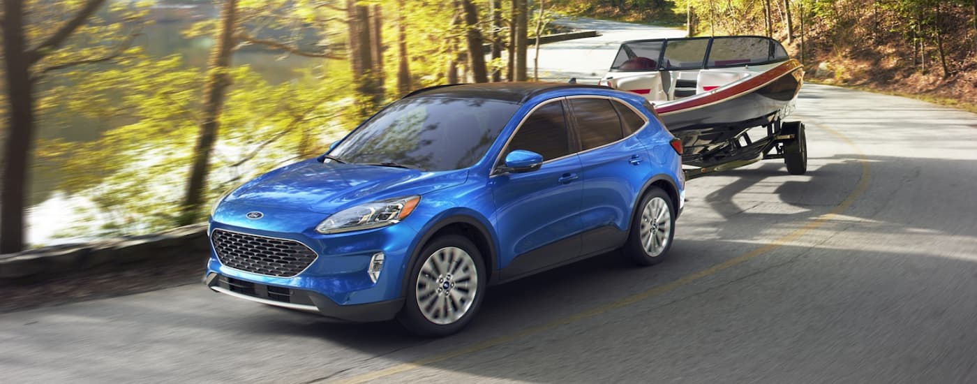 A blue 2020 Ford Escape Hybrid is towing a boat on a winding road.