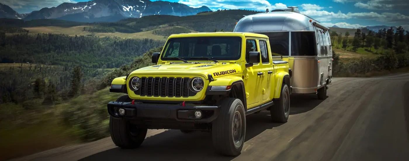 A yellow 2024 Jeep Gladiator Rubicon towing a trailer to a Jeep dealer in Houston.
