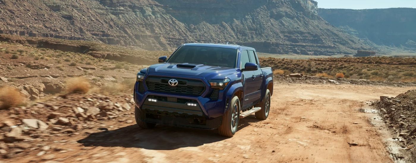 A blue 2024 Toyota Tacoma TRD Sport driving on a dirt trail after leaving a Toyota dealer.