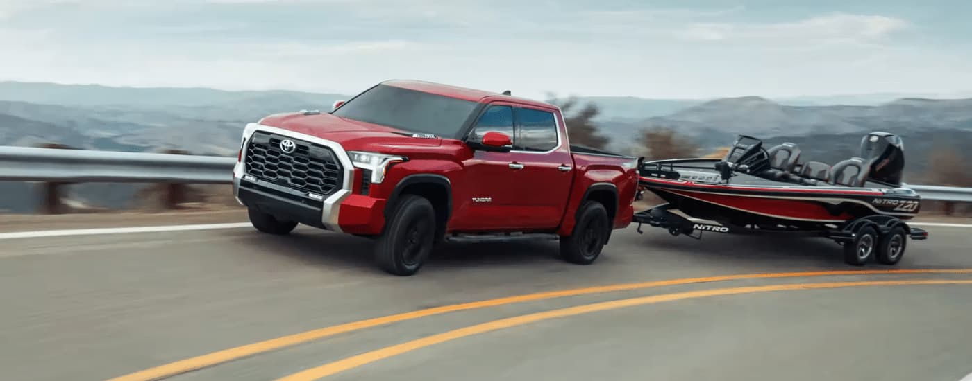 A red 2024 Toyota Tundra towing a boat on a winding road.