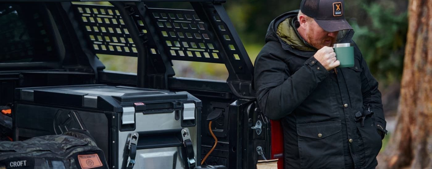 A person is shown leaning against a 2024 Toyota Tacoma Trailhunter drinking from a green mug.