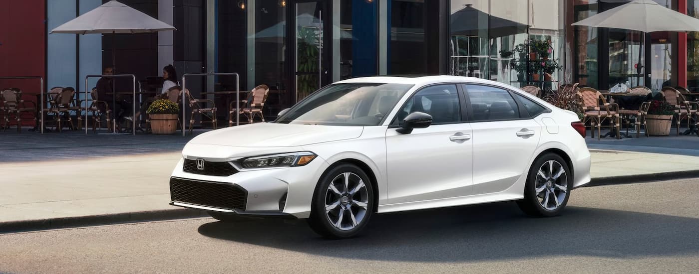 A white 2025 Honda Civic Sport Touring Hybrid parked outside of a cafe.