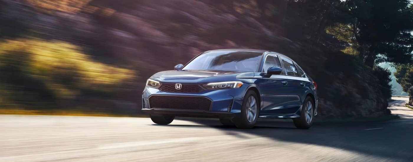 A blue 2025 Honda Civic Hybrid LX is driving on a tree-lined road.