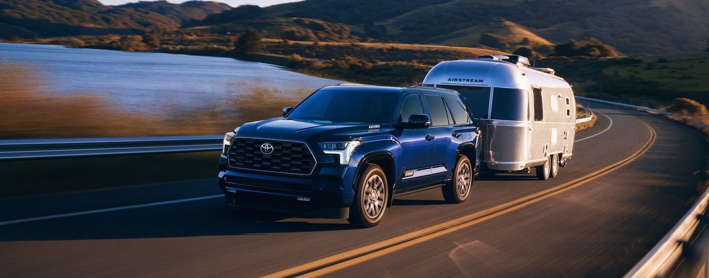 A blue 2024 Toyota Sequoia is shown from the front at an angle while towing an Airstream camper.
